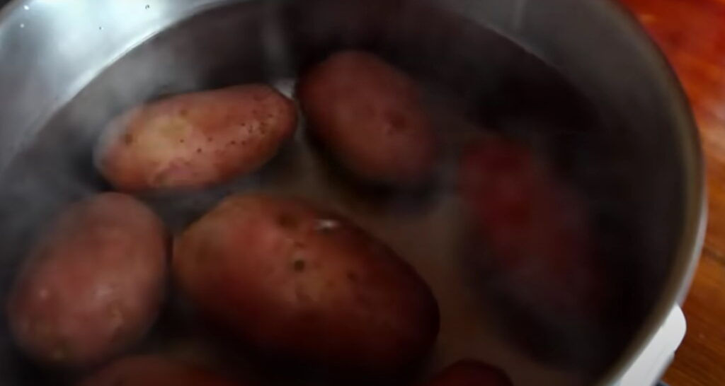 Сира картопля зі шкіркою вариться в каструлі без кришки